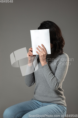 Image of Happy world book day, read to become someone else - woman covering face with book while reading on grey background