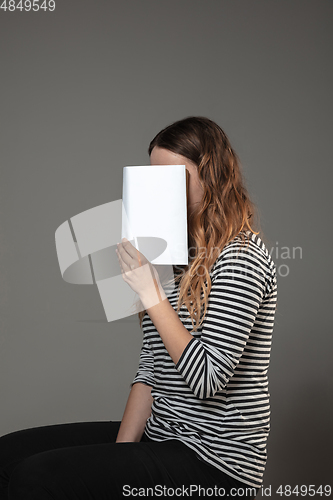 Image of Happy world book day, read to become someone else - woman covering face with book while reading on grey background