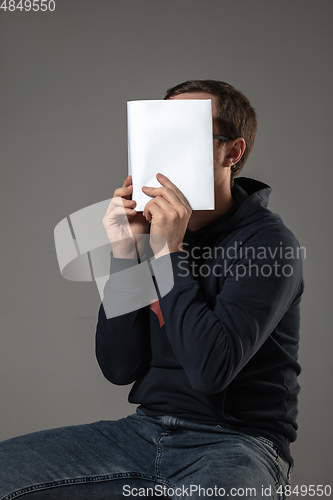 Image of Happy world book day, read to become someone else - man covering face with book while reading on grey background