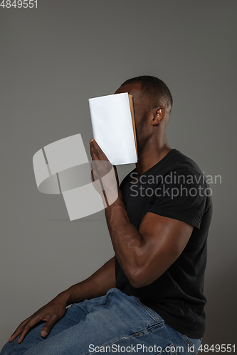 Image of Happy world book day, read to become someone else - man covering face with book while reading on grey background