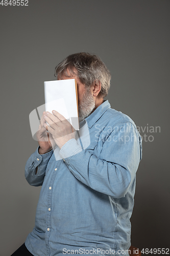 Image of Happy world book day, read to become someone else - man covering face with book while reading on grey background