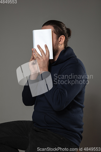 Image of Happy world book day, read to become someone else - man covering face with book while reading on grey background