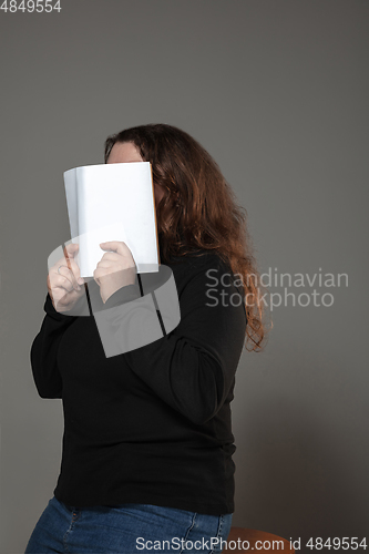 Image of Happy world book day, read to become someone else - woman covering face with book while reading on grey background