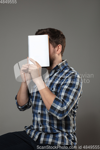 Image of Happy world book day, read to become someone else - man covering face with book while reading on grey background