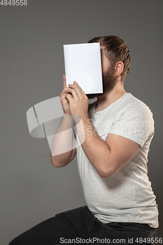 Image of Happy world book day, read to become someone else - man covering face with book while reading on grey background