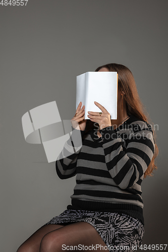 Image of Happy world book day, read to become someone else - woman covering face with book while reading on grey background
