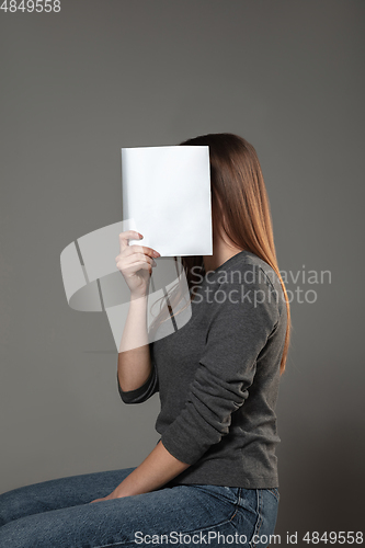 Image of Happy world book day, read to become someone else - woman covering face with book while reading on grey background