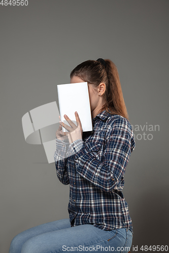 Image of Happy world book day, read to become someone else - woman covering face with book while reading on grey background