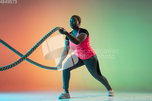 Image of Young african-american plus size female model\'s training on gradient background