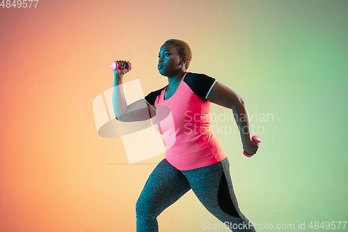 Image of Young african-american plus size female model\'s training on gradient background