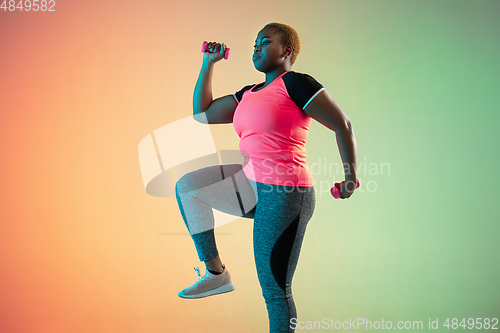 Image of Young african-american plus size female model\'s training on gradient background