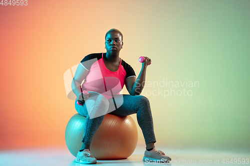 Image of Young african-american plus size female model\'s training on gradient background