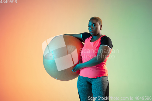 Image of Young african-american plus size female model\'s training on gradient background