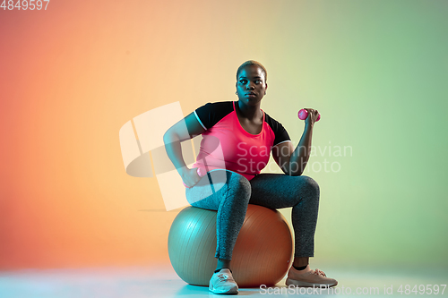 Image of Young african-american plus size female model\'s training on gradient background