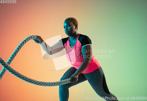 Image of Young african-american plus size female model\'s training on gradient background