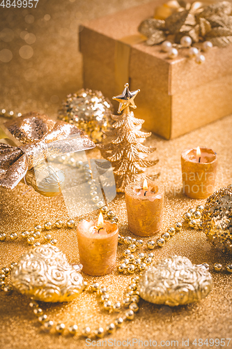 Image of Christmas ornaments, present box and candles in golden tones