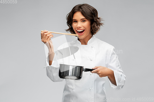 Image of happy female chef with saucepan tasting food