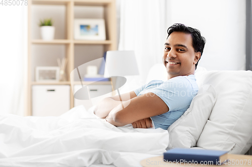 Image of happy smiling indian man lying in bed at home