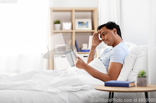 Image of stressed indian man with tablet pc in bed at home
