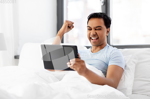 Image of happy indian man with tablet pc in bed at home