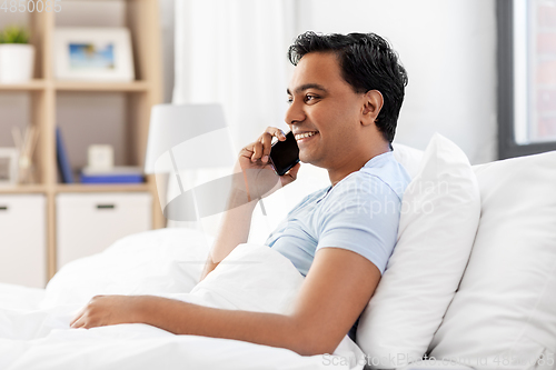 Image of happy indian man calling on smartphone in bed