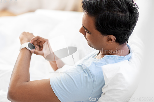 Image of happy indian man with smart watch in bed at home