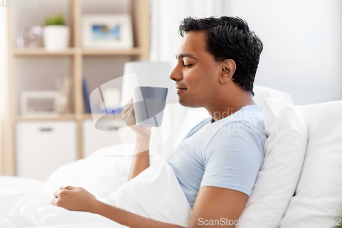 Image of happy indian man drinking coffee in bed at home