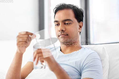 Image of man in bed dropping medicine into glass of water