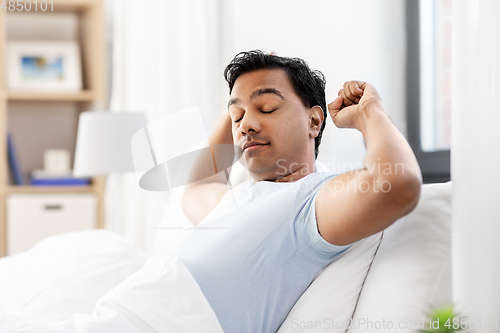 Image of sleepy indian man stretching in bed at home