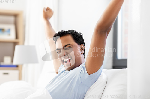 Image of happy smiling indian man lying in bed at home