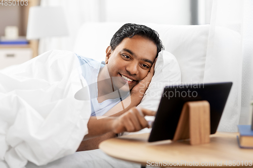 Image of happy indian man with tablet pc in bed at home