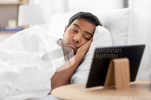 Image of sleepy indian man looking at tablet pc in bed