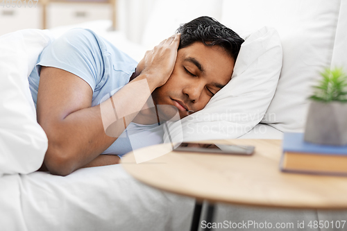 Image of sleepy indian man in bed closing ear with hand