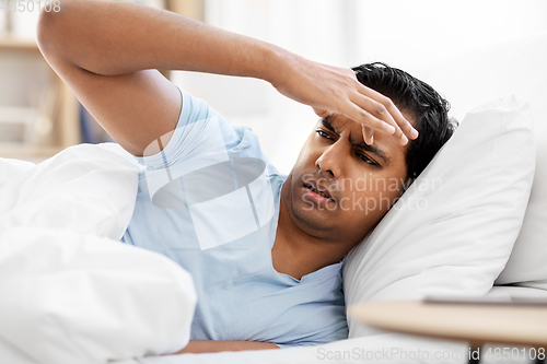 Image of indian man having headache lying in bed at home