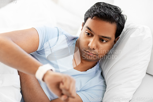 Image of indian man looking at smart watch in bed at home