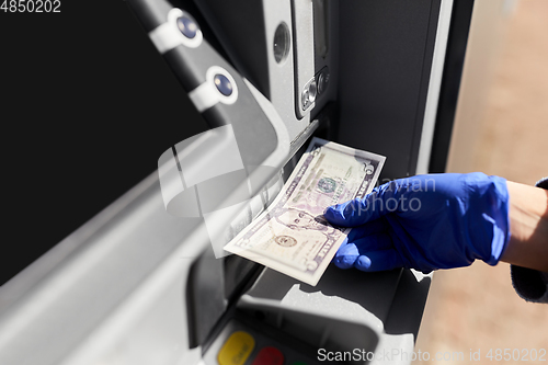 Image of hand in medical glove with money at atm machine