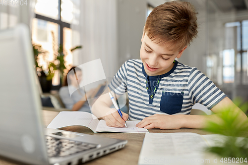 Image of student boy with book writing to notebook at home