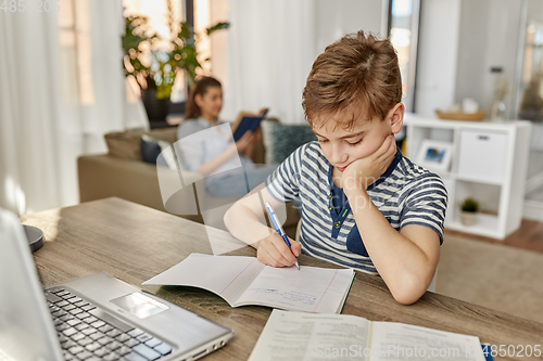 Image of student boy with book writing to notebook at home