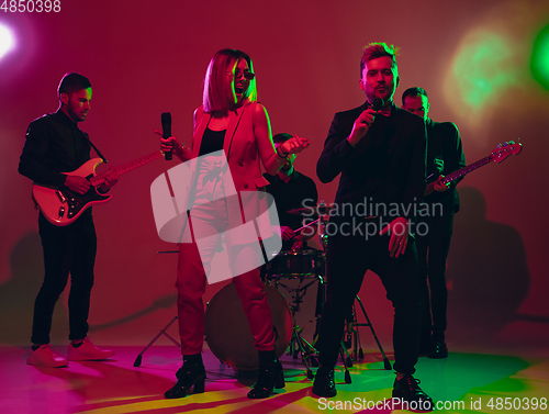 Image of Young caucasian musicians, band performing in neon light on red studio background