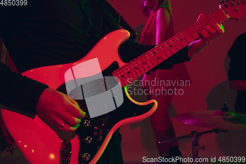 Image of Young caucasian musician, band performing in neon light on red studio background