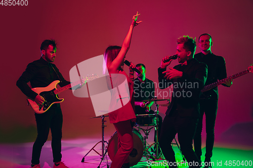 Image of Young caucasian musicians, band performing in neon light on red studio background