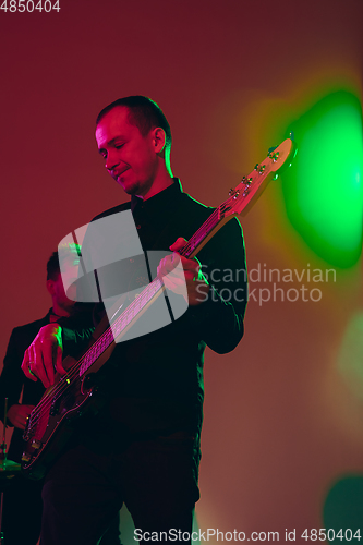 Image of Young caucasian musician, band performing in neon light on red studio background