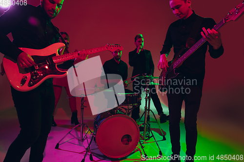 Image of Young caucasian musicians, band performing in neon light on red studio background