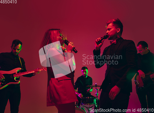 Image of Young caucasian musicians, band performing in neon light on red studio background