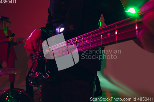 Image of Young caucasian musician, band performing in neon light on red studio background