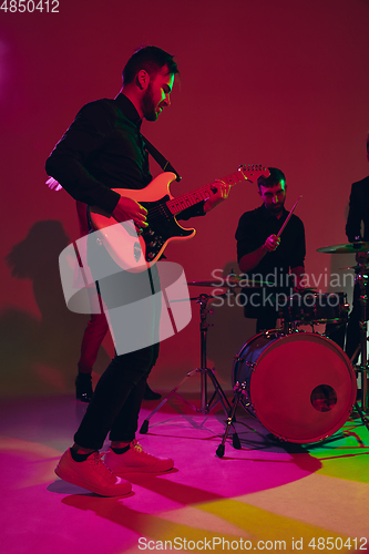 Image of Young caucasian musician, band performing in neon light on red studio background