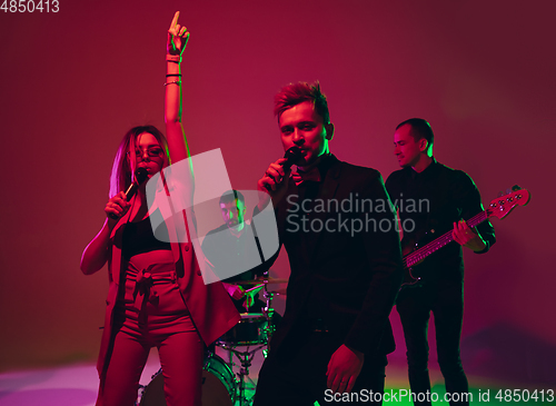 Image of Young caucasian musicians, band performing in neon light on red studio background