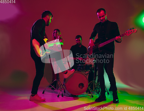 Image of Young caucasian musicians, band performing in neon light on red studio background