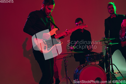 Image of Young caucasian musicians, band performing in neon light on red studio background