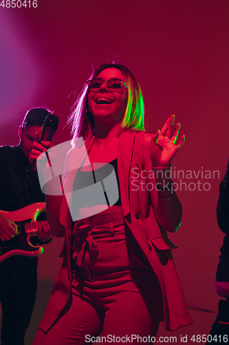 Image of Young caucasian musician, singer performing in neon light on red studio background